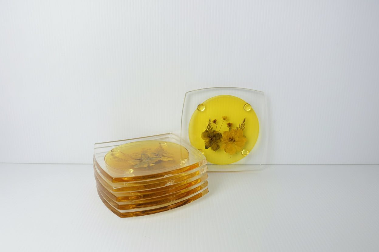 Set of six yellow coasters with floral design on a white background